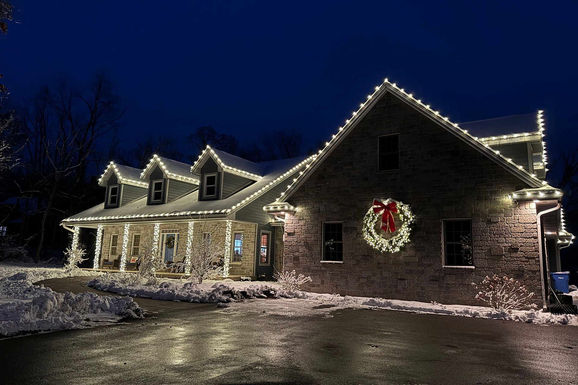 Snow-covered house decorated with Christmas lights and a wreath at night
