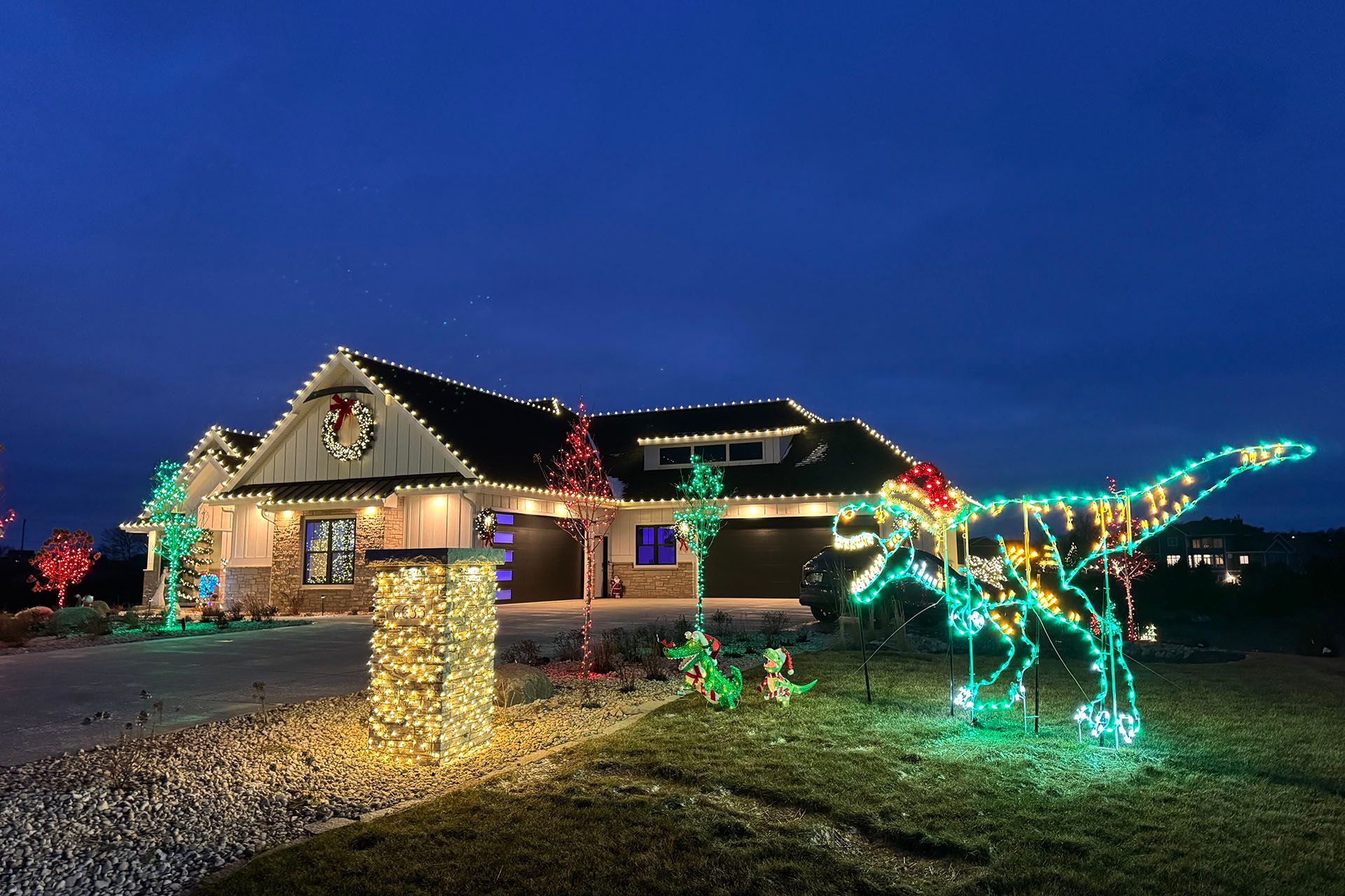 House and yard lit with colorful Christmas lights, including a glowing reindeer at dusk