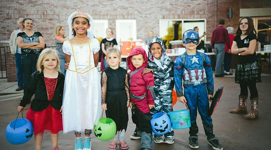 Costumed children with pumpkin buckets standing together outdoors at Halloween event