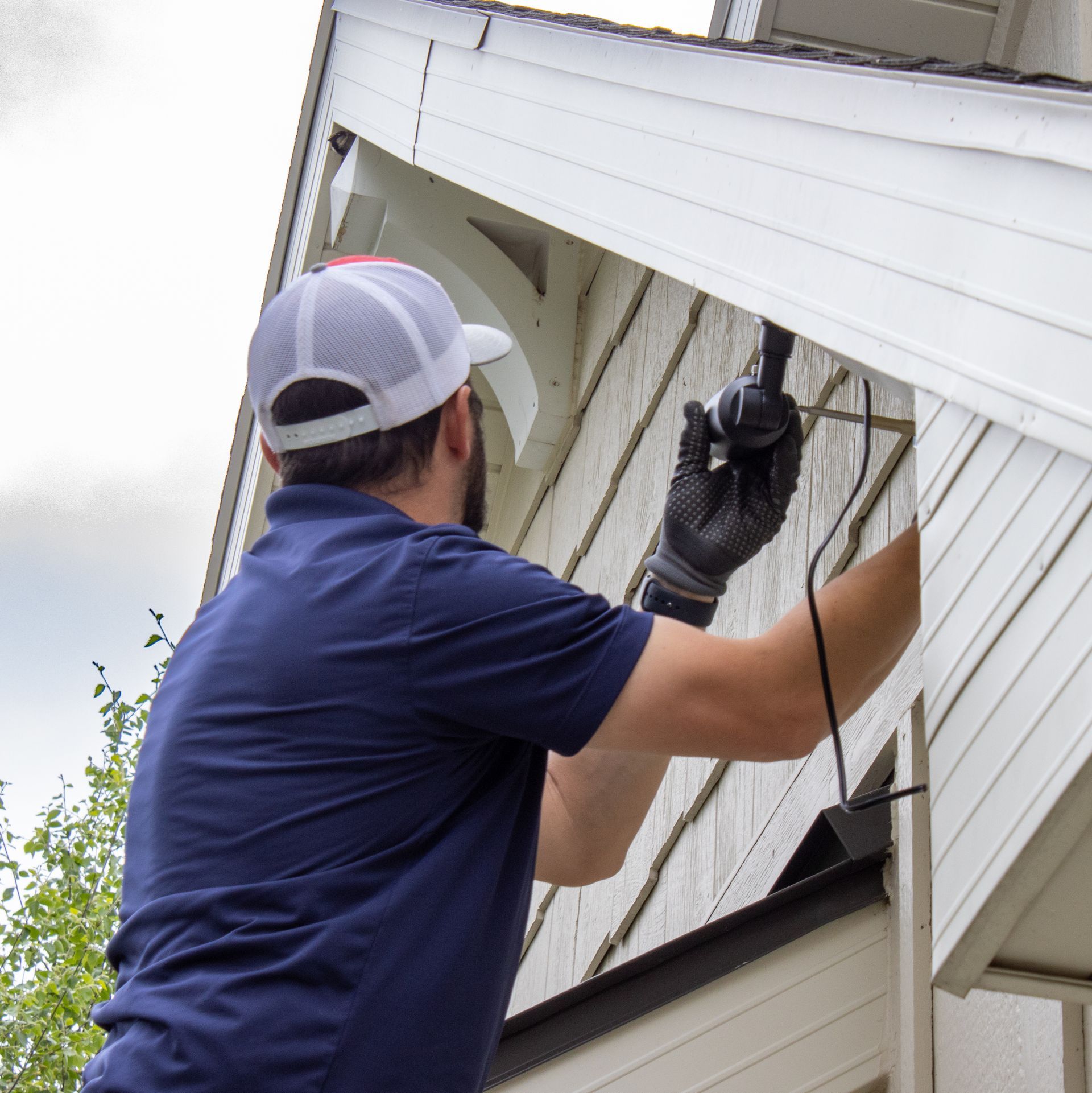 Worker cleaning an exterior house window with a squeegee and hose under the roof eave