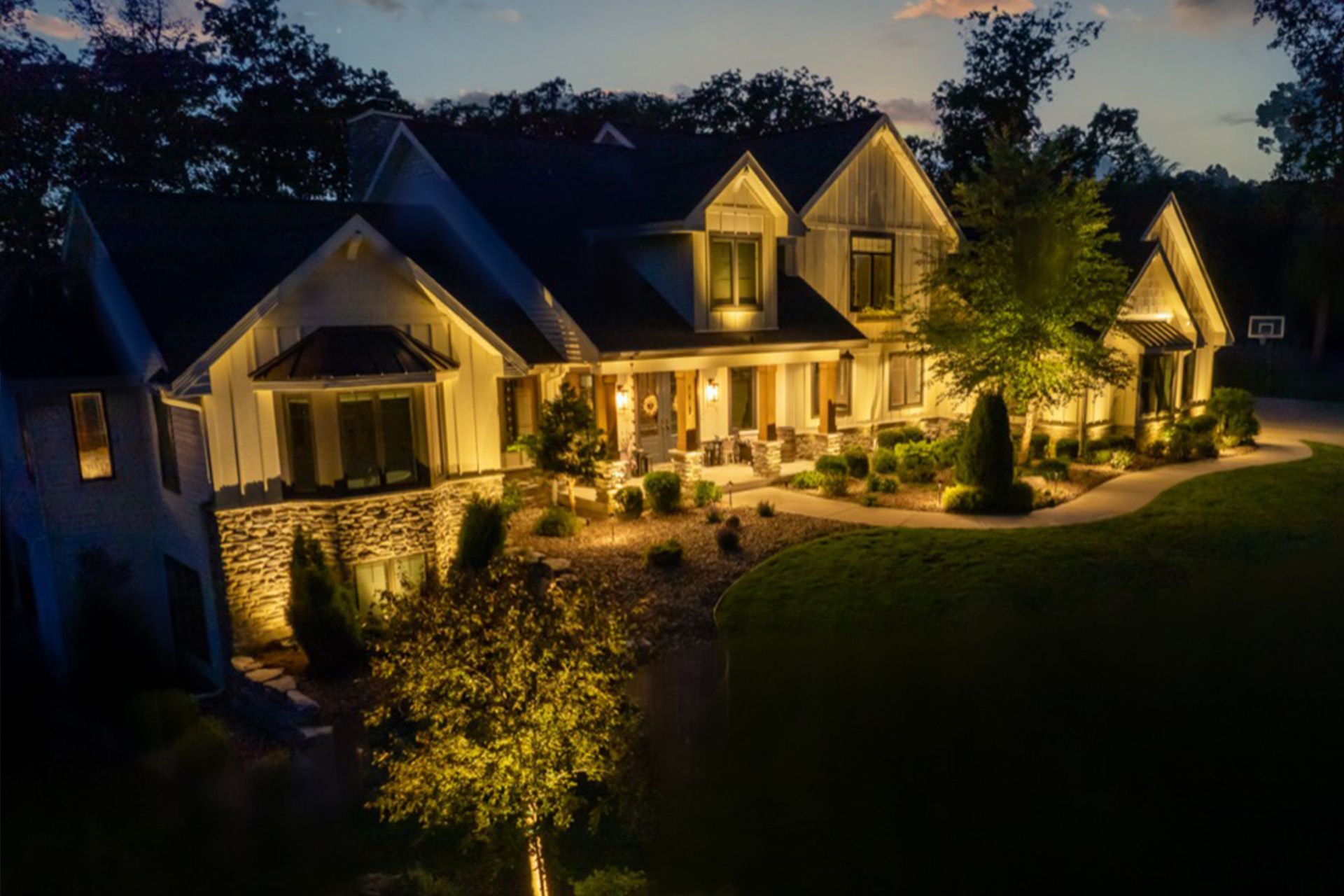 Luxurious house at dusk with warm exterior lighting and landscaped front yard