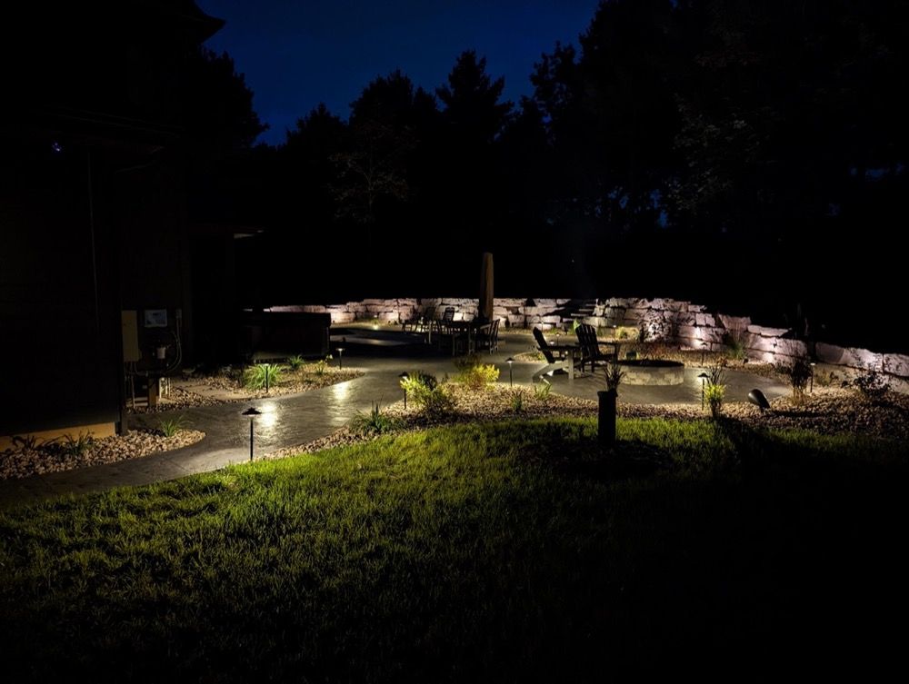 Nighttime landscaped garden with lit pathways, rocks, and trees reflected in water