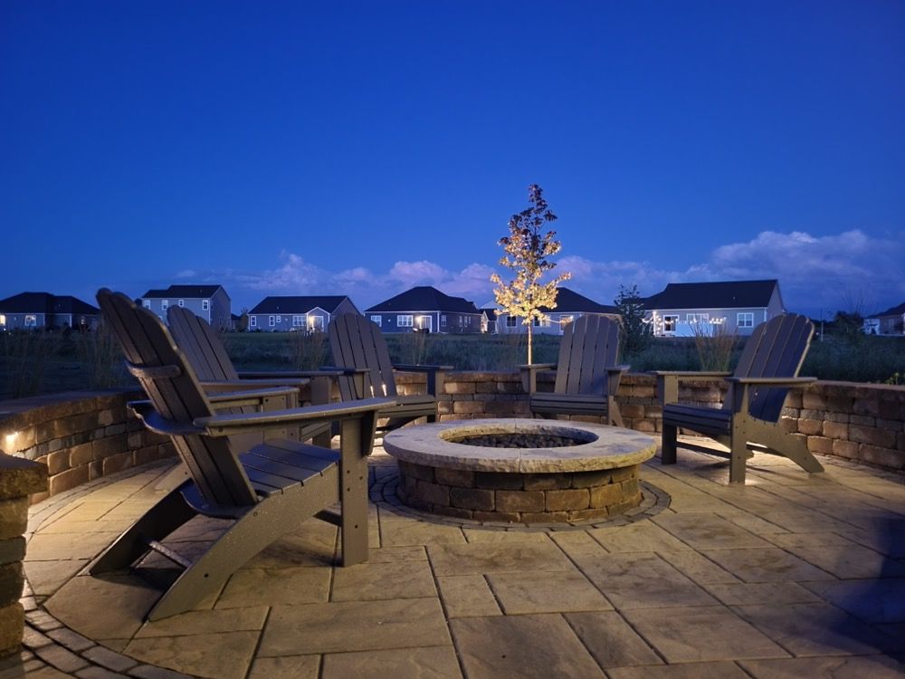 Backyard stone fire pit seating area at dusk with lit tree and blue sky