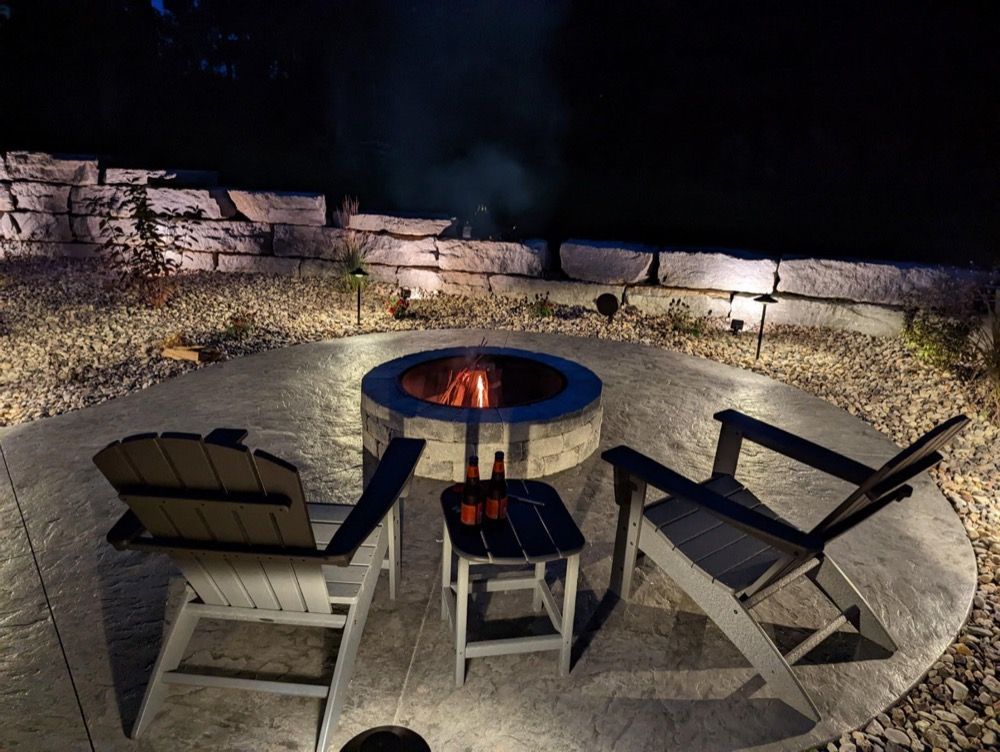 Outdoor patio with fire pit and three chairs at night