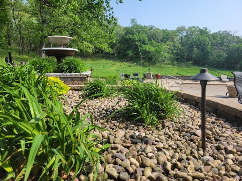 Landscaped garden with stone riverbed, fountain, and a paved path beside green trees