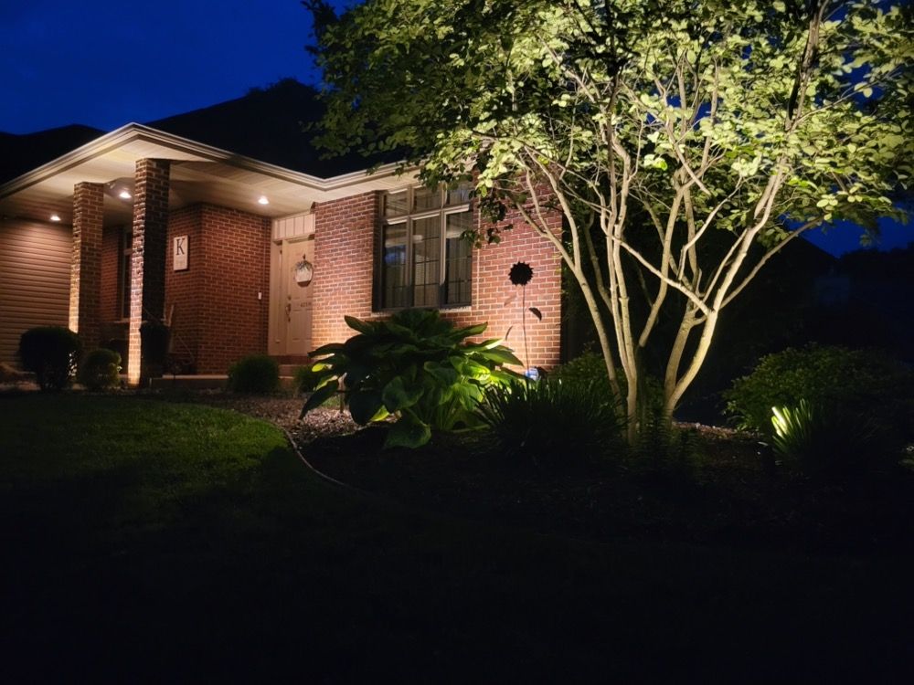 Brick house at night with warm porch lights and a lit tree in the front yard