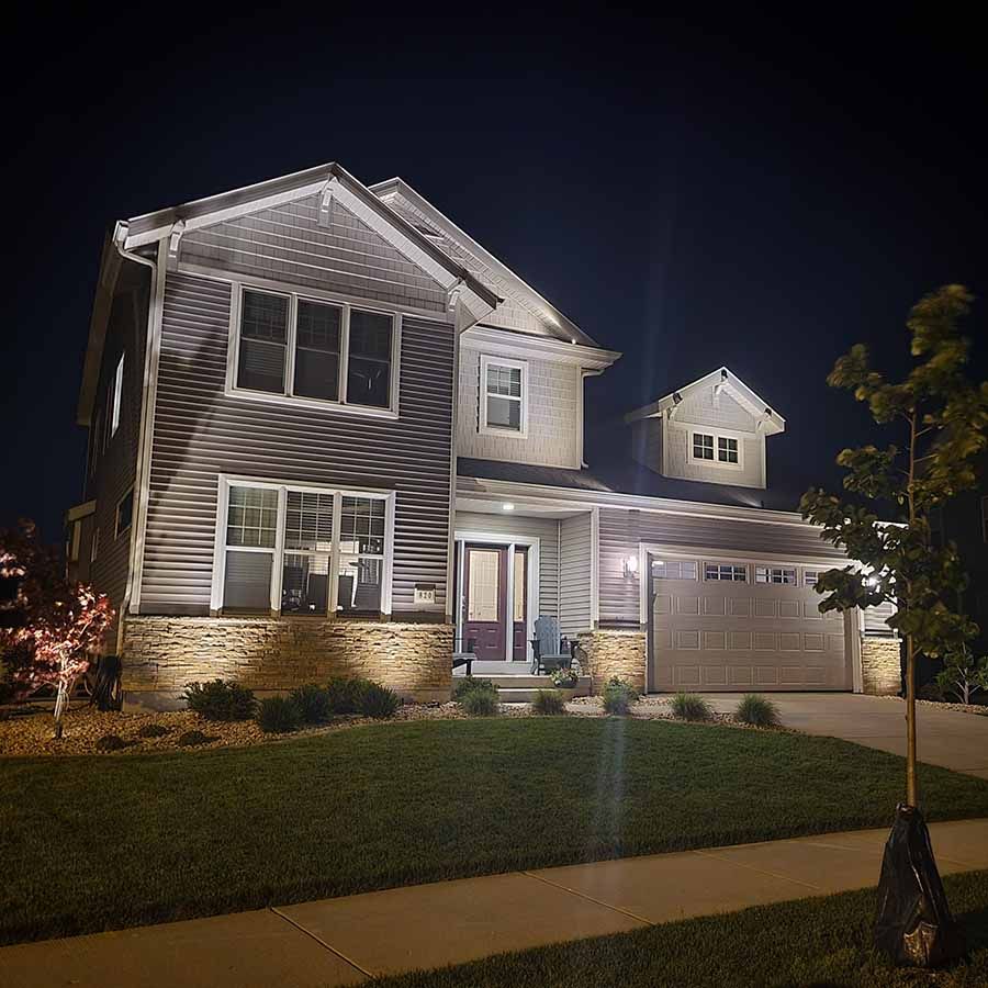 Two-story suburban house at night, lit from the outside, with a garage, lawn, and front walkway.