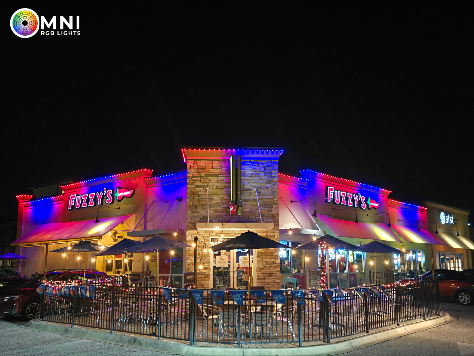 Neon-lit restaurant exterior at night with outdoor seating and parked cars