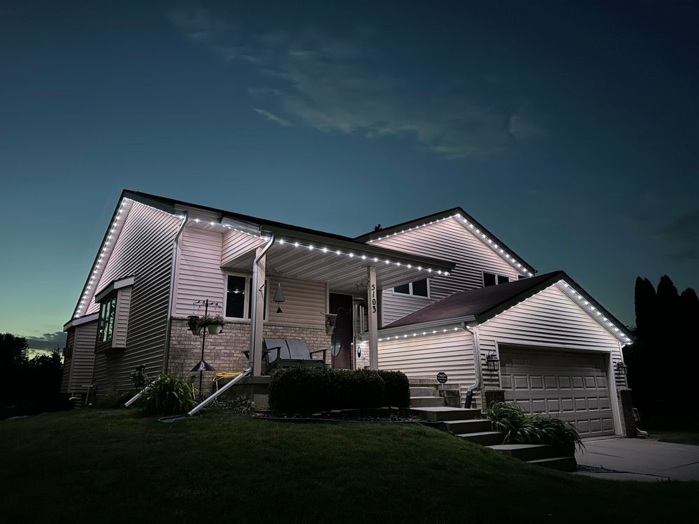 Nighttime view of a white suburban house with lit windows and a detached garage under a dark sky