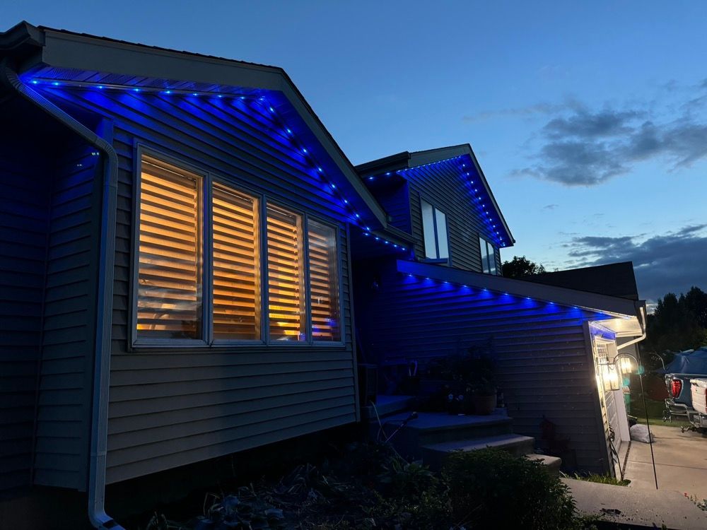 House at dusk with blue roof lights and warm glowing windows under a cloudy sky