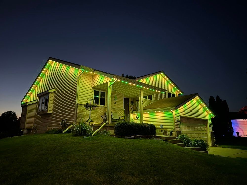 House lit with green and yellow lights at night on a grassy hill