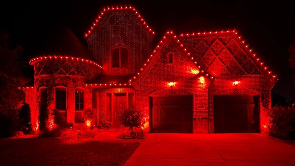 House covered in red holiday lights at night, with glowing rooflines and a brightly lit driveway