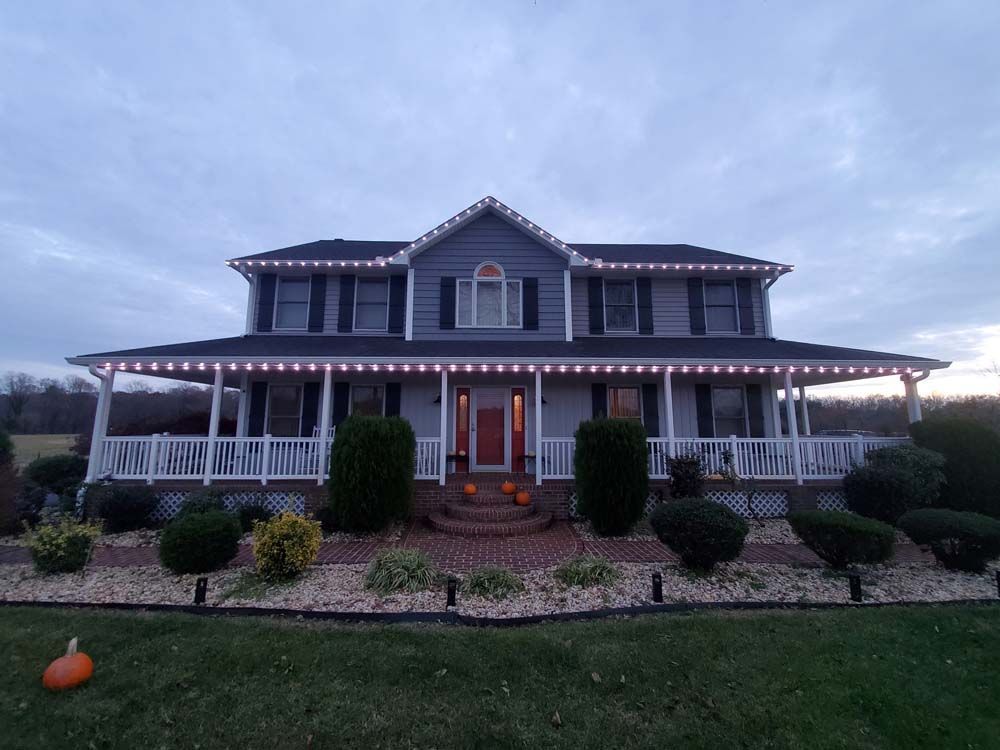 Two-story gray house with a wraparound porch and lit red door at dusk