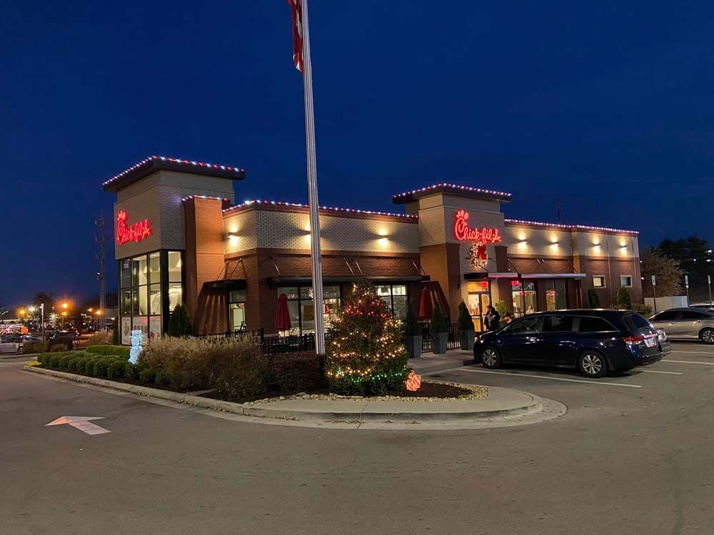 Chick-fil-A restaurant at dusk with red signage, lit windows, and cars parked outside.