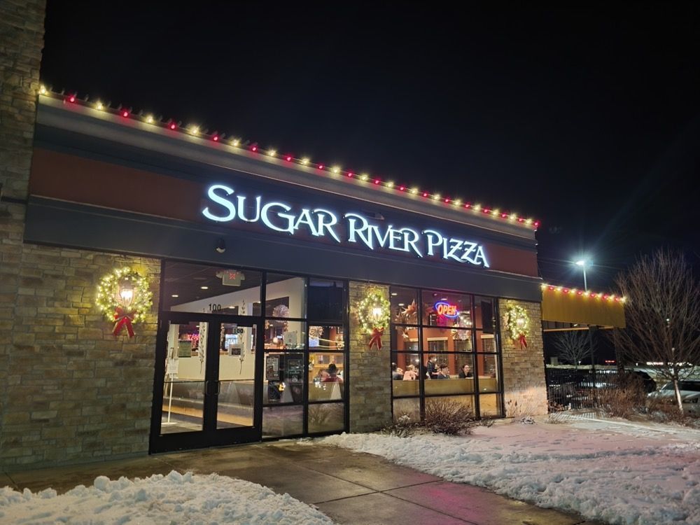 Sugar River Pizza storefront at night, lit sign above snow-covered entrance.