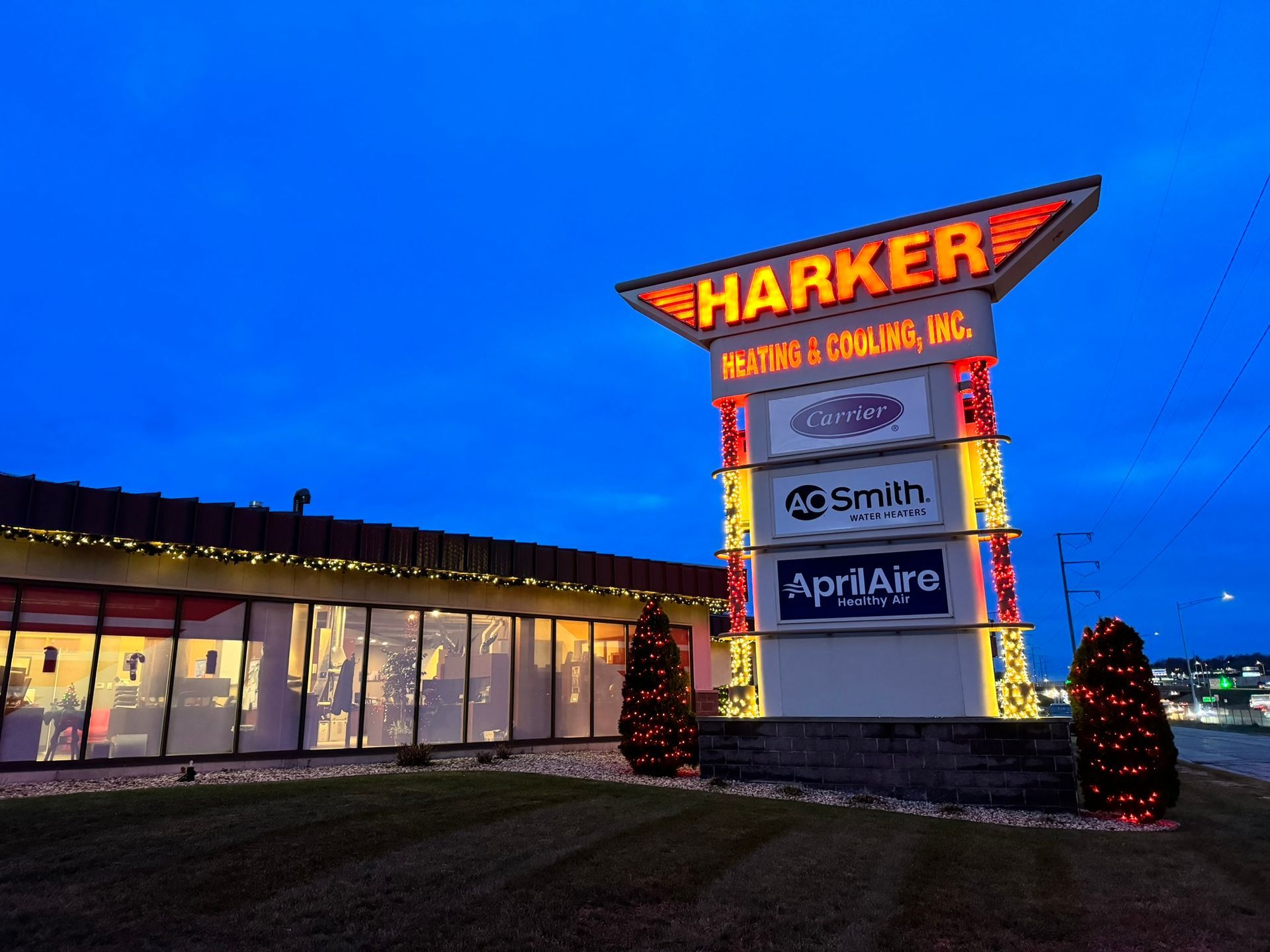 Harker sign illuminated at dusk outside a dealership building, with blue sky and holiday lights
