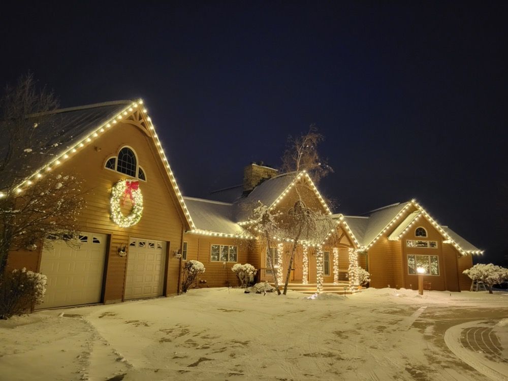 Snowy house decorated with warm Christmas lights and a wreath at night