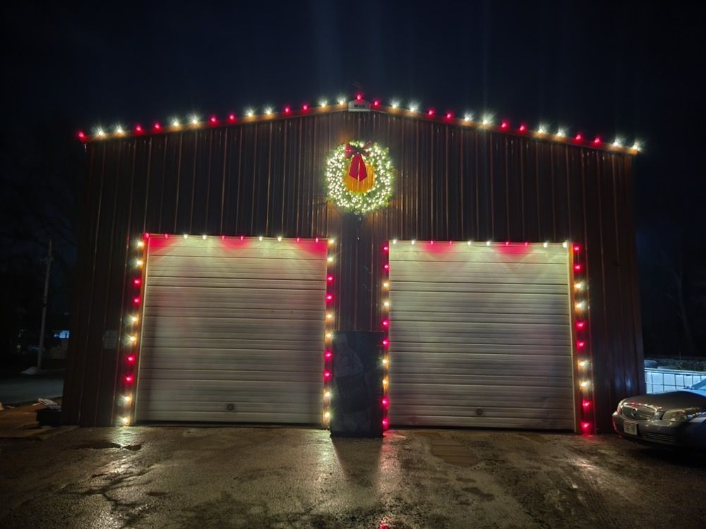 Building with two garage doors outlined in colorful Christmas lights and a wreath above, at night