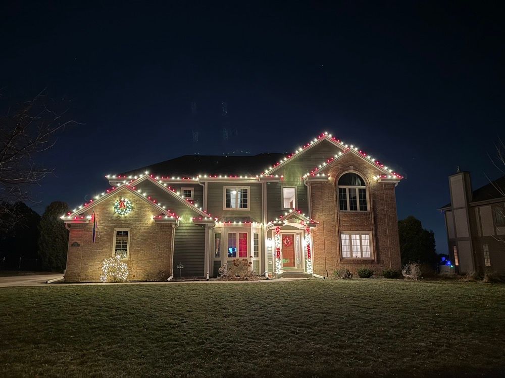 Brick house decorated with colorful Christmas lights at night on a grassy lawn