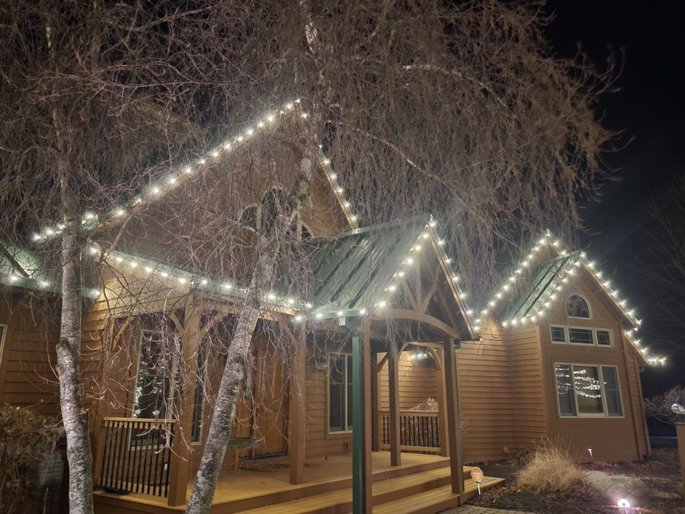 Lit log cabin at night with festive white string lights and bare trees in front