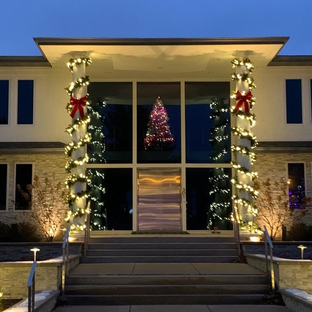 Front entrance of a building lit with holiday garlands and a decorated Christmas tree inside at night