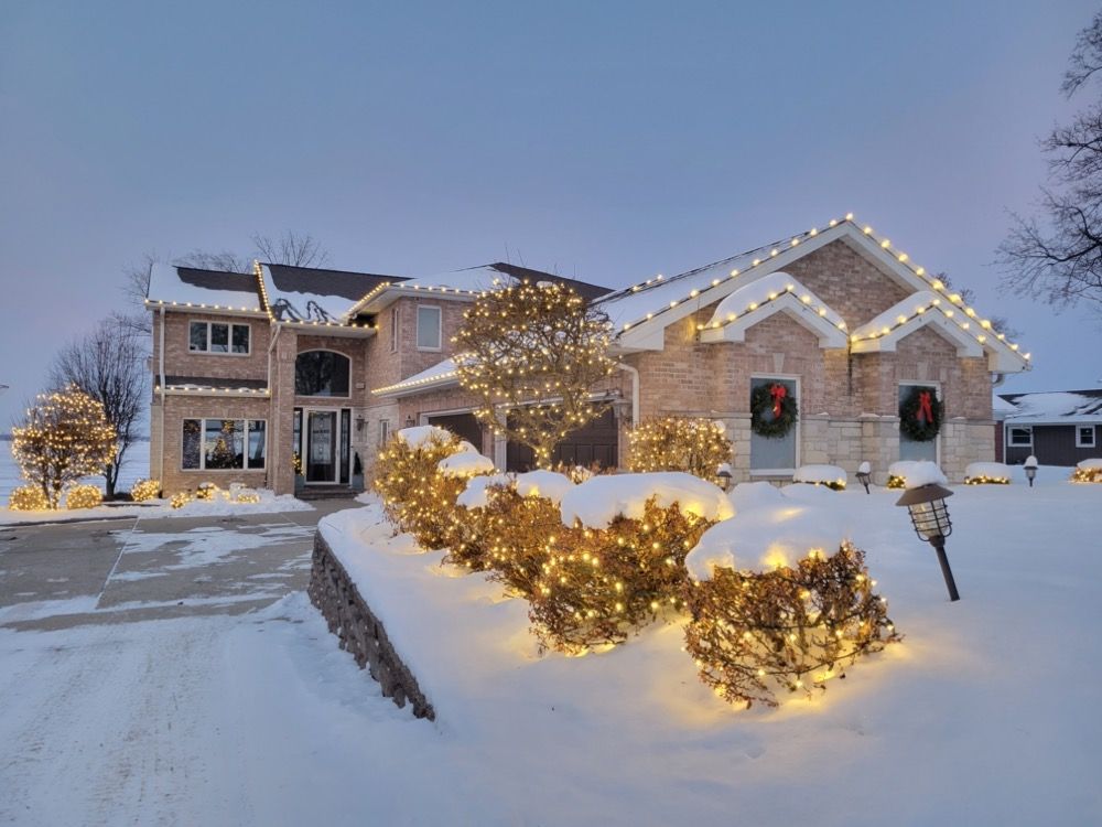 Snow-covered suburban house with warm holiday lights and wreaths at dusk