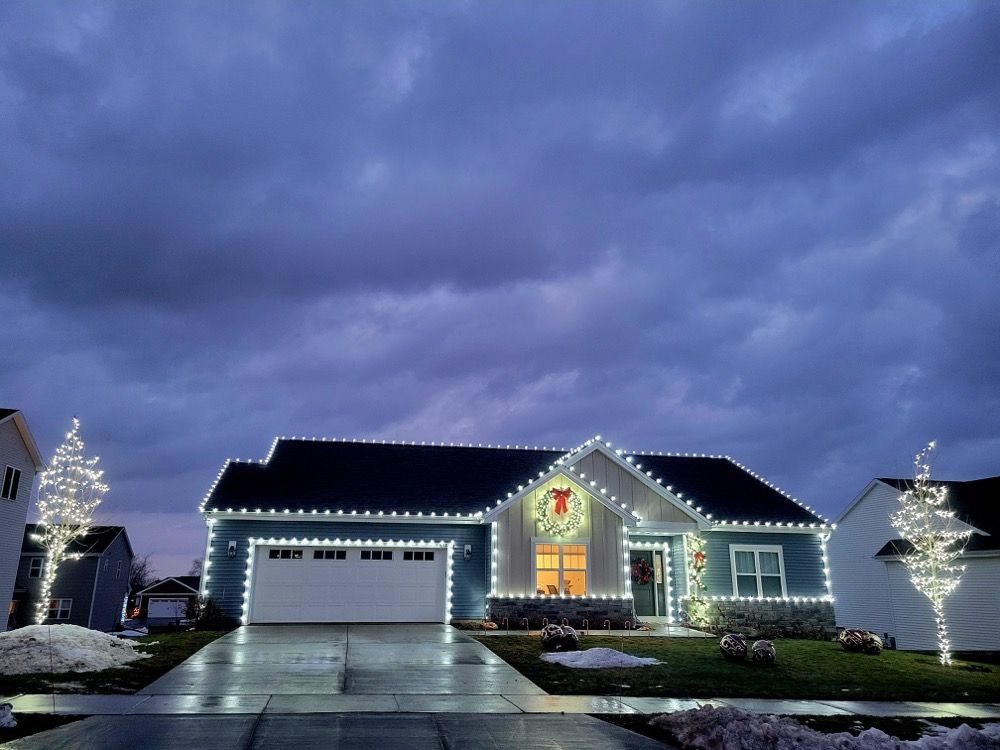 Suburban house at dusk with Christmas lights and decorations, reflecting on a wet driveway under a cloudy sky