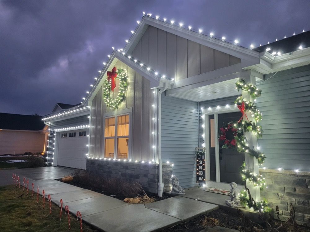 House exterior decorated with white Christmas lights and wreaths at dusk