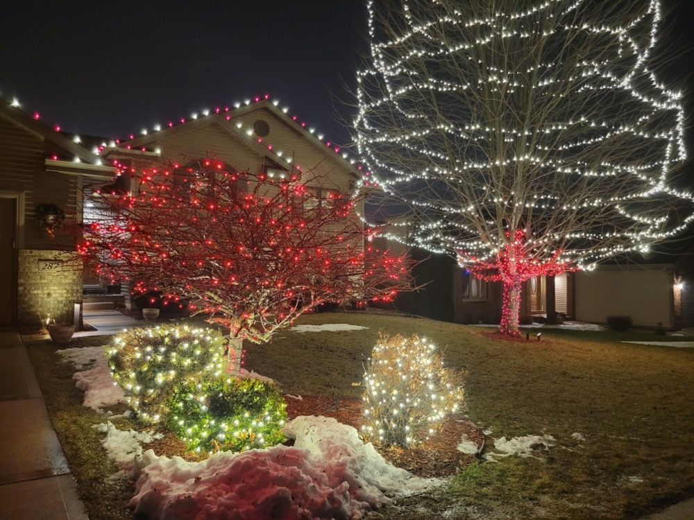 Holiday-lit suburban house with red and white glowing trees and snowy yard decorations at night