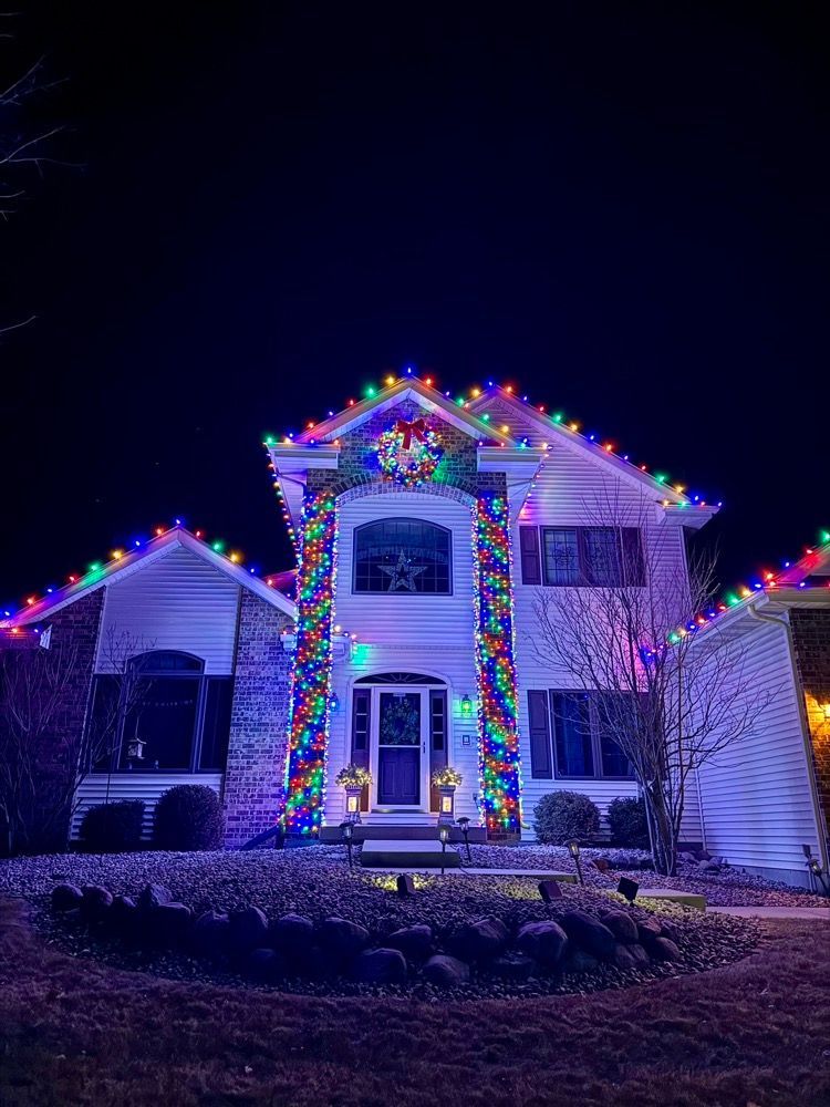 House decorated with colorful Christmas lights at night, glowing against a dark sky.