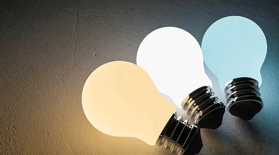 Three light bulbs glowing in warm, white, and blue tones on a dark background