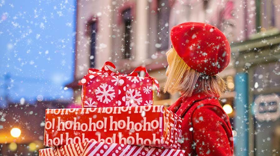 Woman in red winter clothing carrying a large “ho ho ho” gift box in falling snow