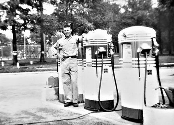 A black and white photo of a man standing next to gas pumps