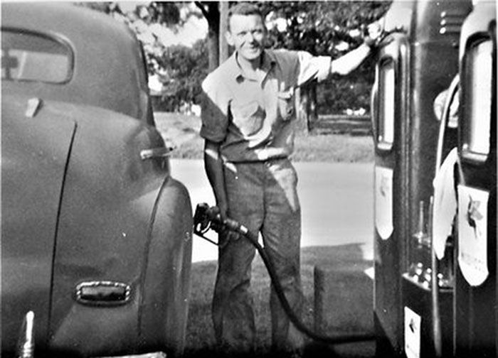 A black and white photo of a man pumping gas into a car