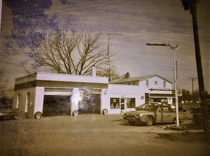 A black and white photo of a gas station with cars parked in front of it