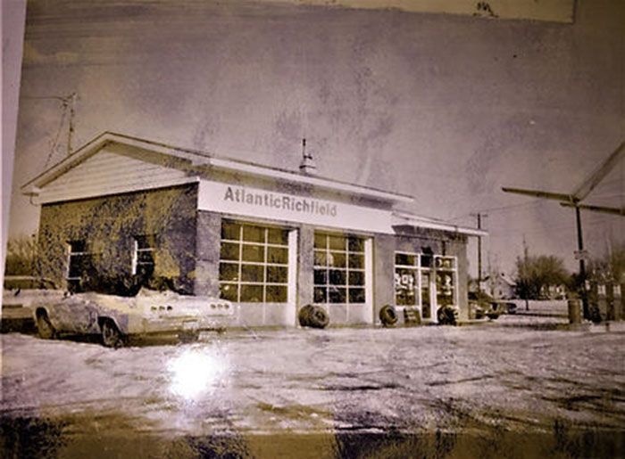A black and white photo of a gas station with a car parked in front of it.