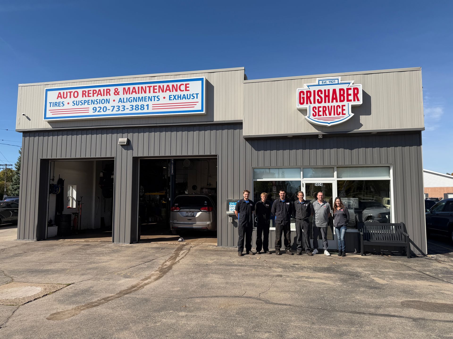 Auto repair and maintenance shop with open garage bays and a group standing outside the storefront.