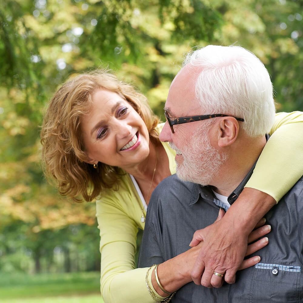 Two smiling people hugging outdoors in a green park