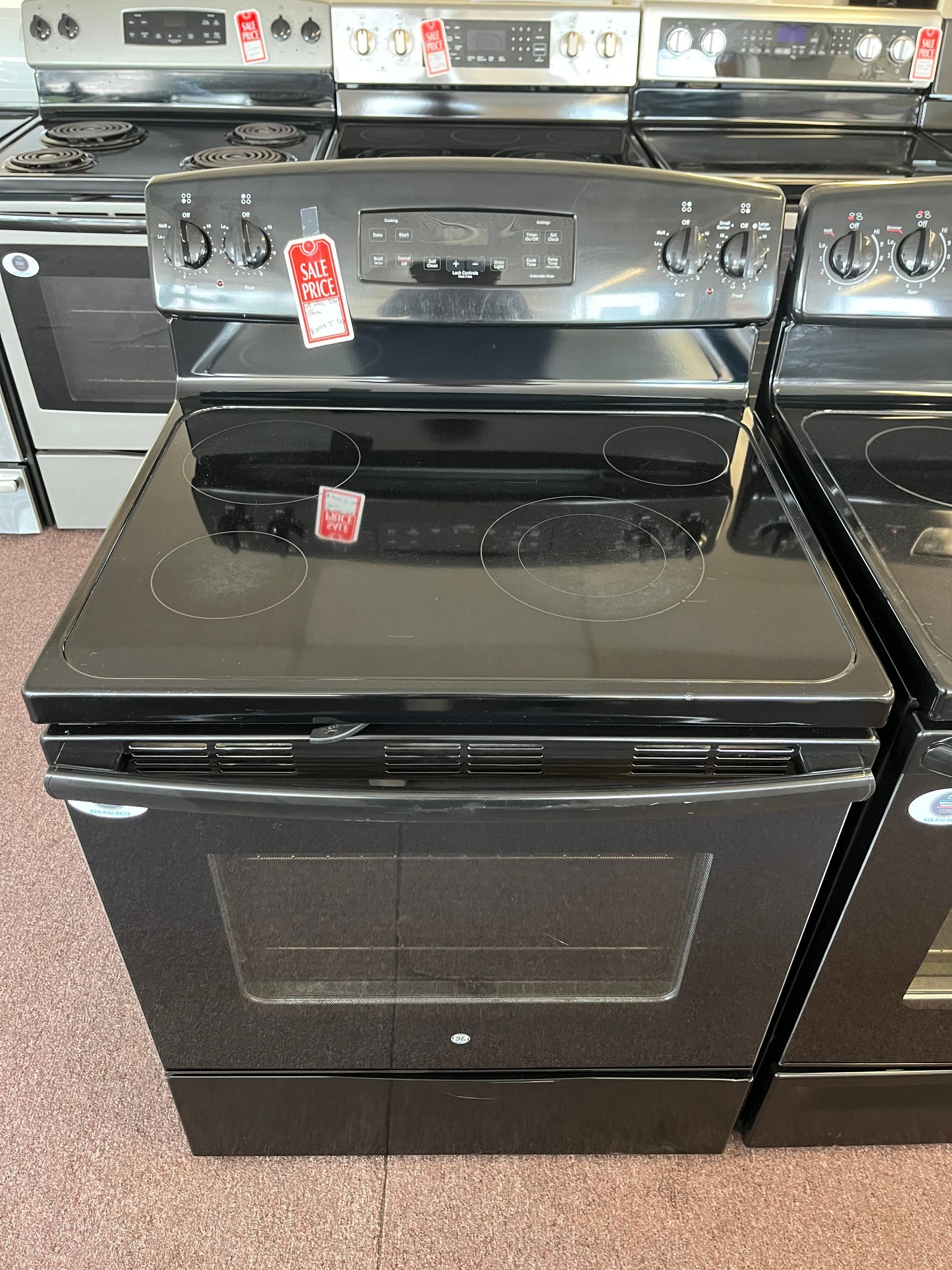 Black electric oven on a showroom floor with a red sale tag and stainless control panel underneath.