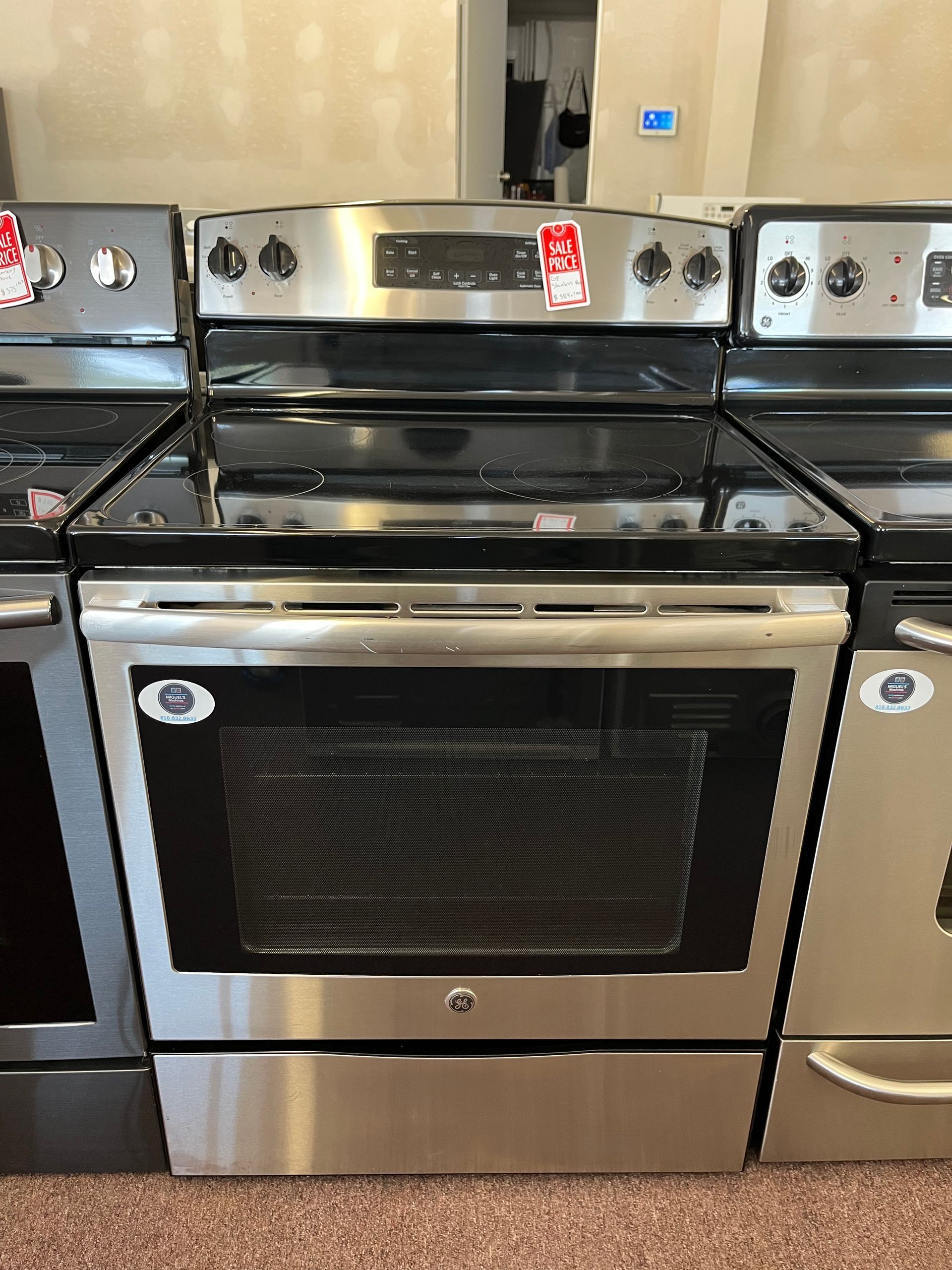Stainless steel stove with black glass oven door in a kitchen, centered between other appliances.