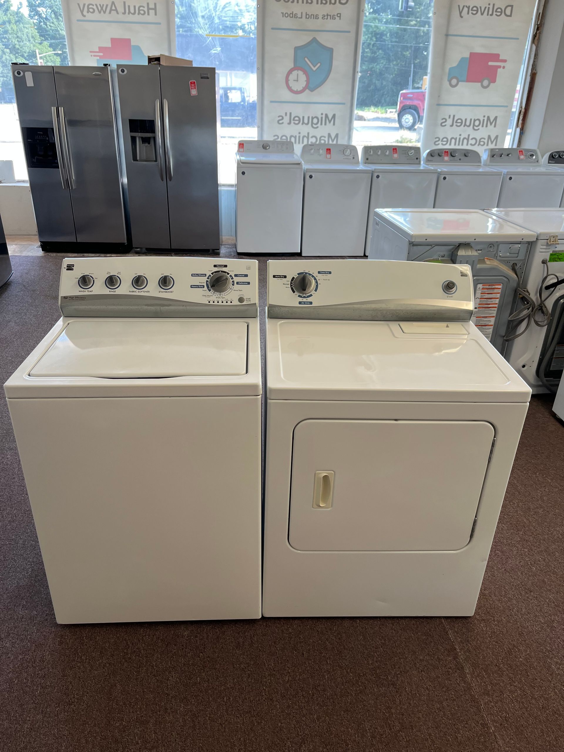 Laundry room with a white washer and dryer side by side under detergent dispensers and windows.