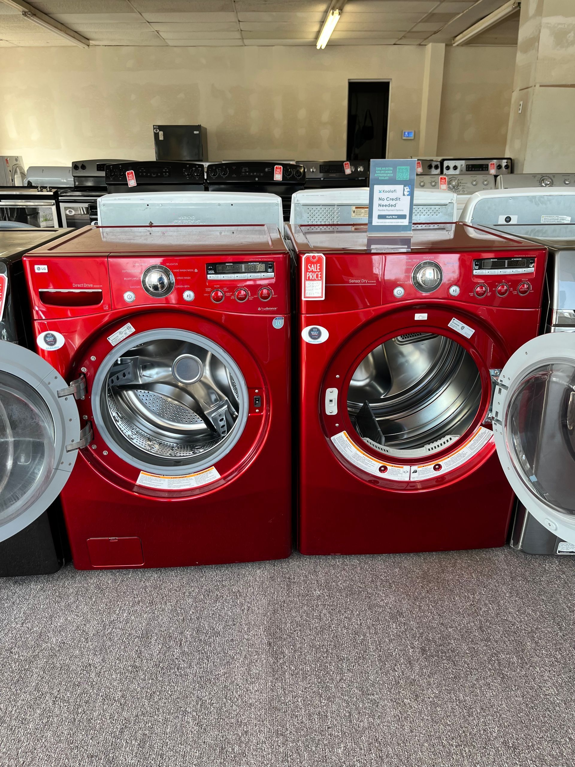 Red washing machines in a laundromat, with one door open and two bins in front.