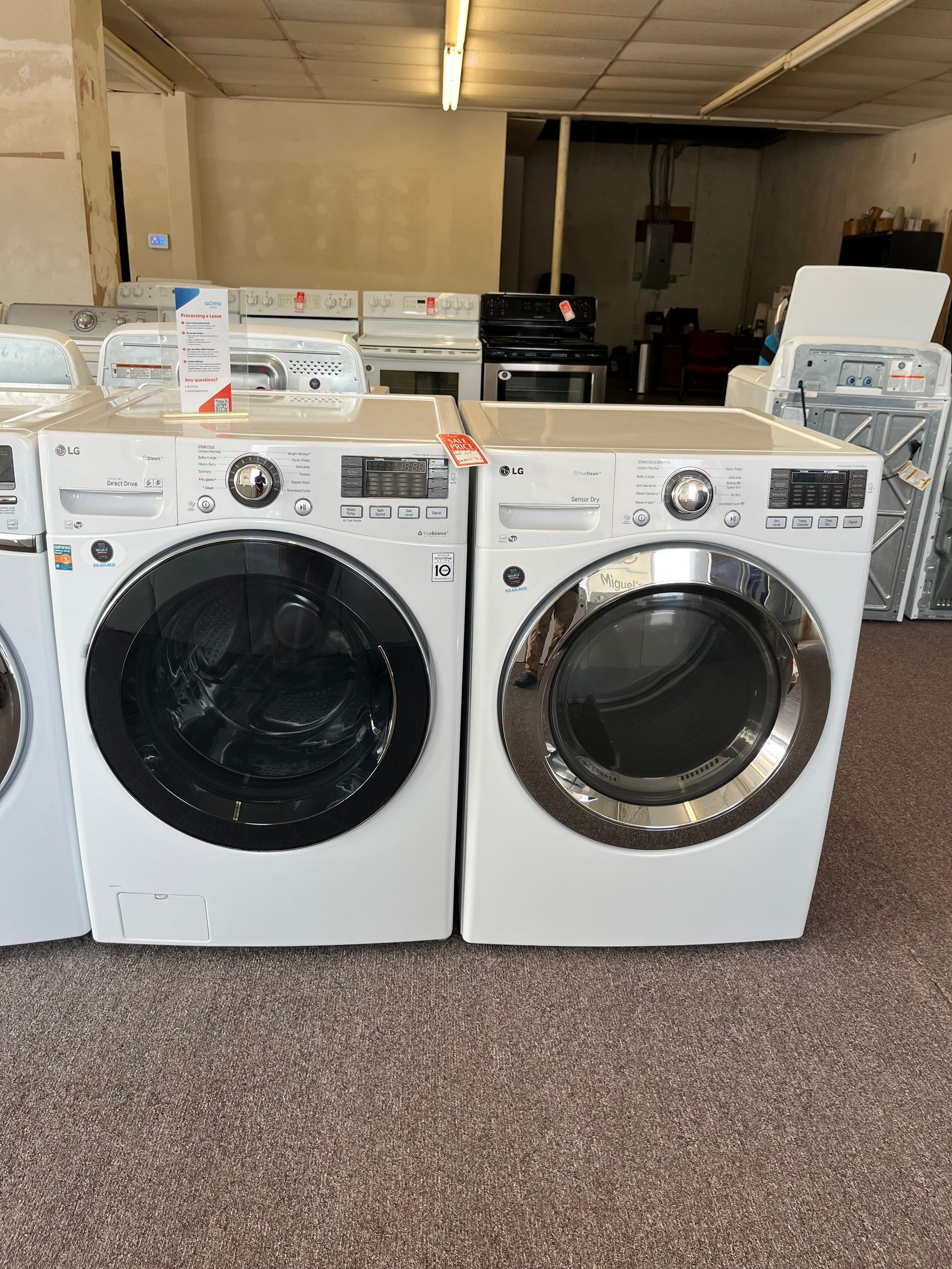 Two white front-load laundry machines in a carpeted showroom or basement laundry area