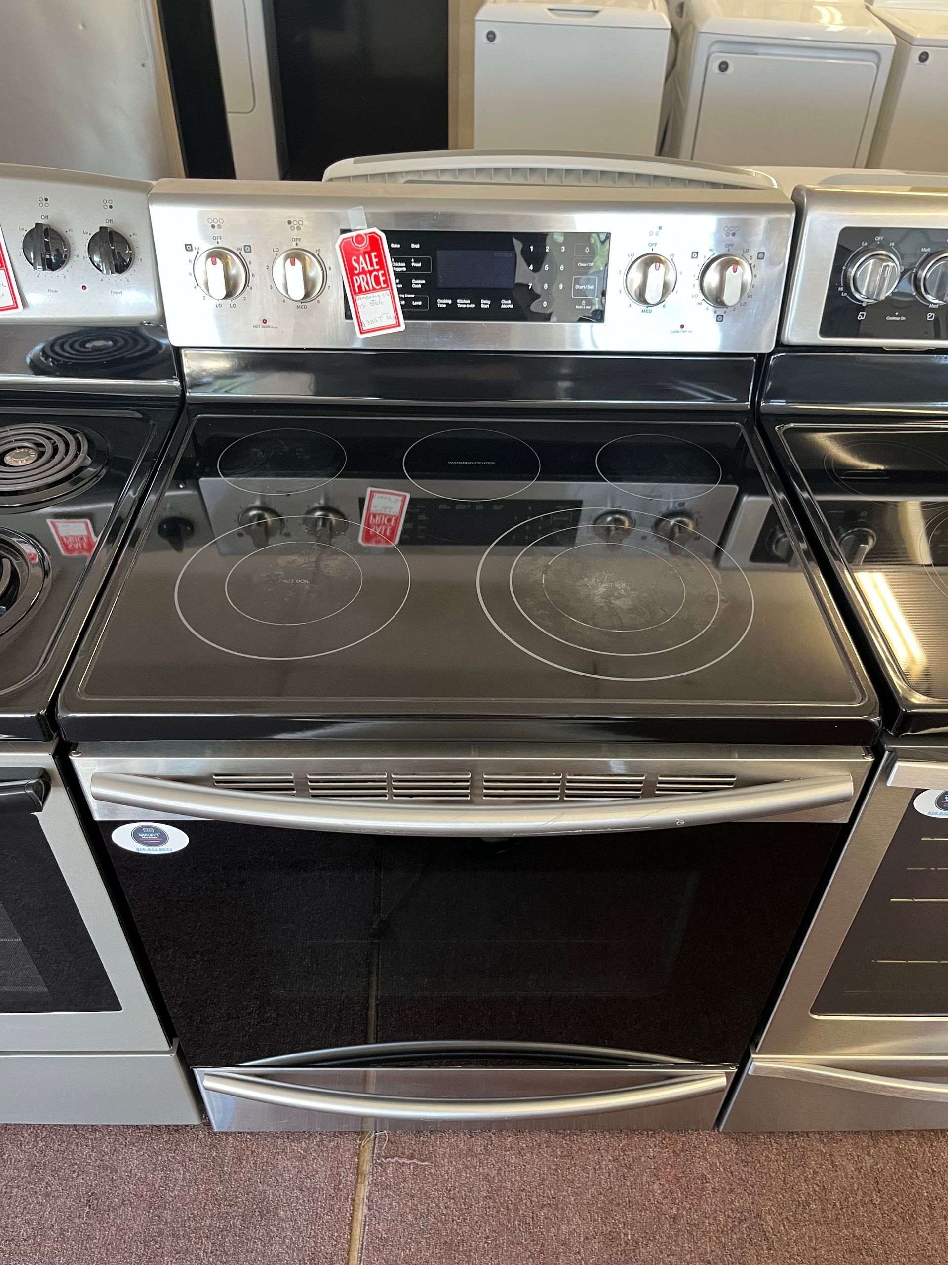 Silver front-load LG washing machine in a laundry appliance showroom, with a dark glass door.