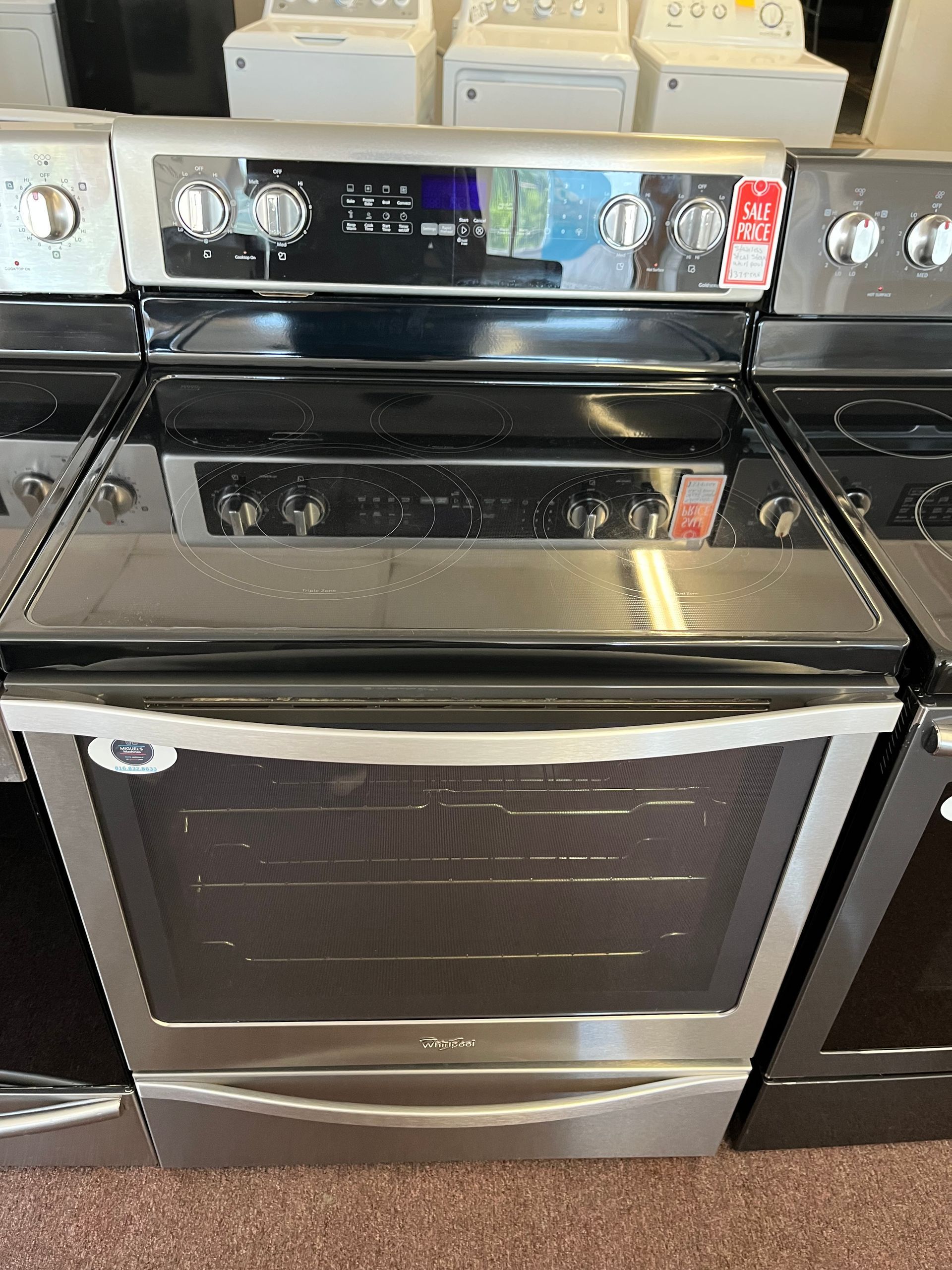 White top-loading washer with control panel, displayed in an appliance store aisle.
