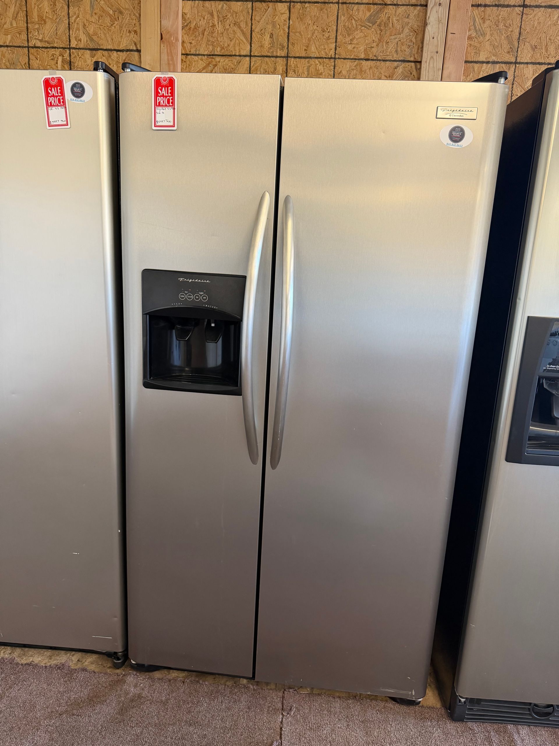 Three stainless steel refrigerators, one with a water dispenser, lined up in a store display.