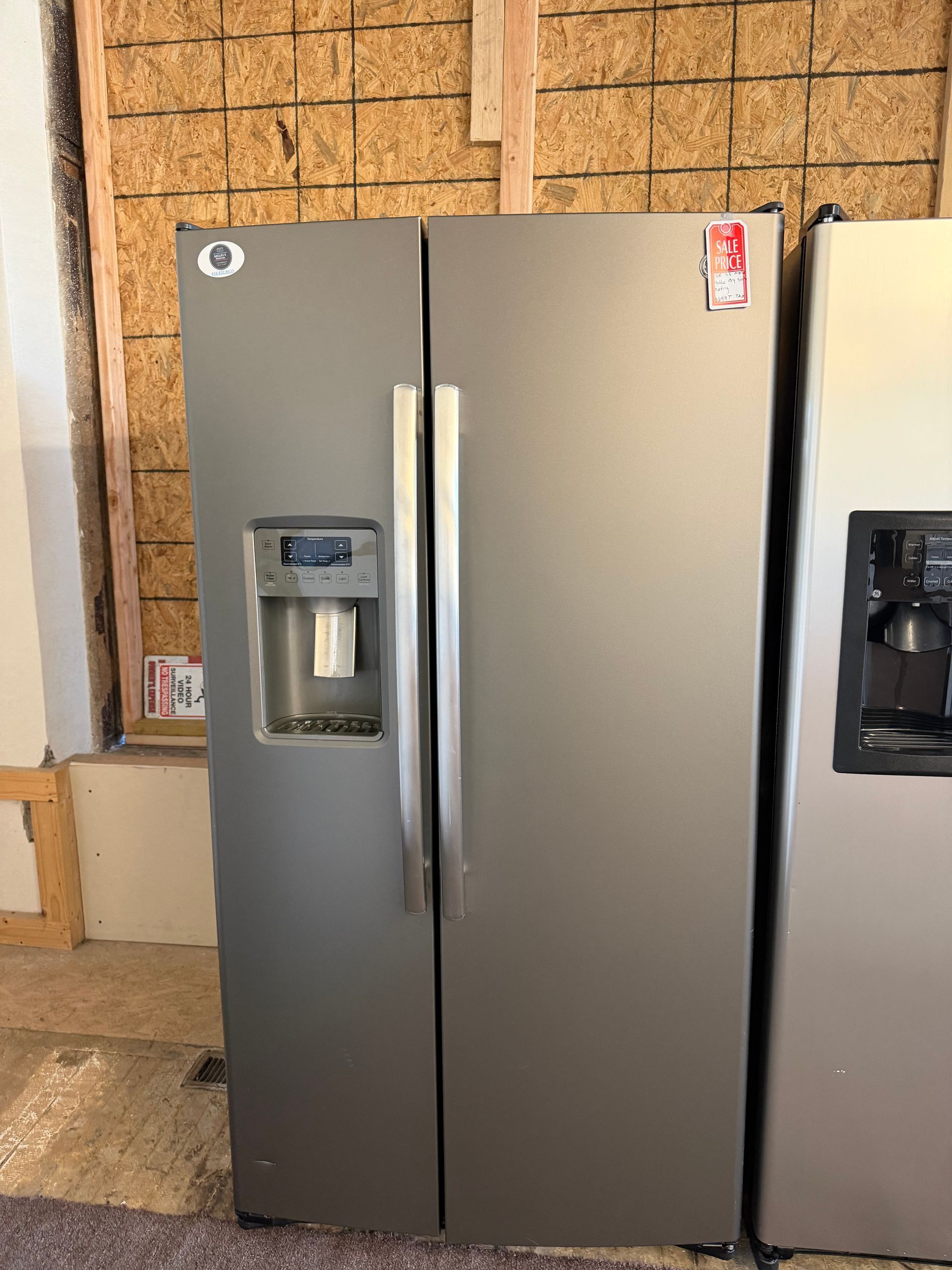 Stainless steel side-by-side refrigerator with water and ice dispensers against a wood-paneled wall.