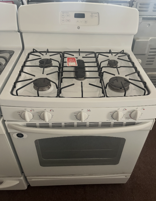 A white GE gas range with a five-burner stovetop, black iron grates, and a digital display on the back control panel.