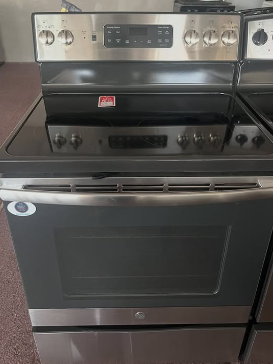 Stainless steel electric range oven with black glass door and control knobs, shown in a kitchen.