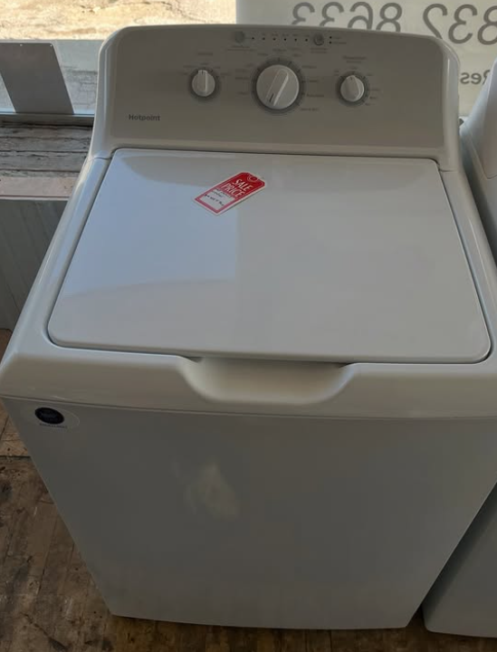 White top-load washing machine with three control knobs, viewed indoors.